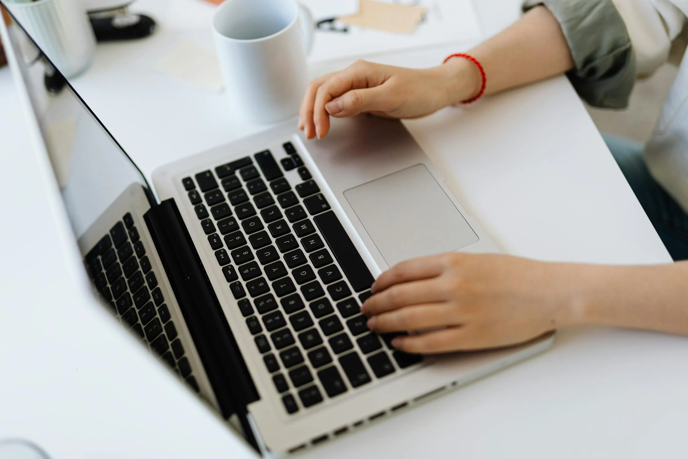 A woman working on a laptop at a white table.